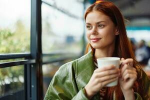 Portrait of a woman influencer drinking a drink from a mug in a cafe and smiling looking out the window, content blogger close-up photo