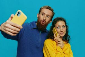 Woman and man funny couple with phones in hand taking selfies crooked smile fun, on blue background. The concept of real family relationships, talking on the phone, work online. photo