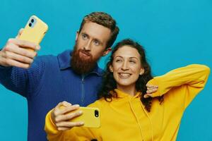 Woman and man funny couple with phones in hand taking selfies crooked smile fun, on blue background. The concept of real family relationships, talking on the phone, work online. photo