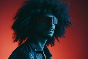 Portrait of fashion man with curly hair on red background with stylish glasses, multicultural, colored light, black leather jacket trend, modern concept. photo