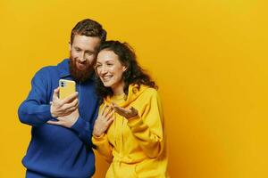 Man and woman couple smiling merrily with phone in hand social media viewing photos and videos, on yellow background, symbols signs and hand gestures, family freelancers.