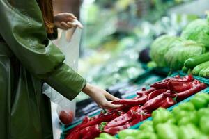 Woman in the grocery store picking fresh vegetables to cook in the supermarket for cooking at home for dinner, shopping at the market red peppers in hand photo