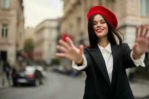 Fashion woman smile with teeth standing on the street in front of the city tourist follow me stylish clothes with red lips and red beret, travel, cinematic color, retro vintage style, urban fashion. photo