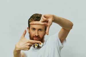 Portrait of a funny man in a white T-shirt with flowers daisies in his beard on a white isolated background, copy place. Holiday concept and congratulations. photo