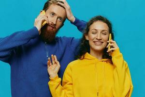 mujer y hombre alegre Pareja con Los telefonos en su manos torcido sonrisa alegre, en azul antecedentes. el concepto de real familia relaciones, hablando en el teléfono, trabajo en línea. foto