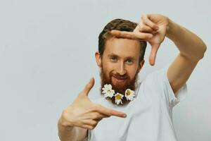 Portrait of a funny man in a white T-shirt with flowers daisies in his beard on a white isolated background, copy place. Holiday concept and congratulations. photo