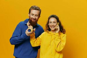 Woman and man cheerful couple with phones in hand talking on cell phone crooked smile cheerful, on yellow background. The concept of real family relationships, talking on the phone, work online. photo