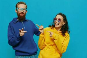 un mujer y un hombre divertido Pareja arrancando y demostración señales con su manos sonriente alegremente, en un azul fondo, el concepto de un real relación en un familia. foto