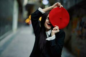 Fashion woman smile with teeth and fun tourist in stylish clothes in jacket and red beret walking down narrow city street flying hair, travel, French style, cinematic color, retro style. photo