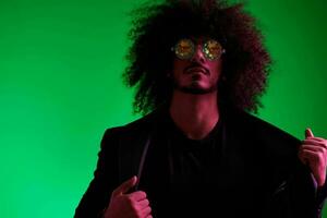 Fashion portrait of a man with curly hair on a green background with sunglasses, multinational, colored pink light, trendy, modern concept. photo