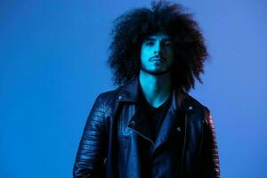 Portrait of fashion man with curly hair on blue background multinational, colored light, black leather jacket trend, modern concept. photo