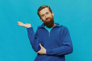 Portrait of man redheaded man with beard in sweater smile and happiness, hand signs and symbols, on blue background. Lifestyle positive, copy place. photo