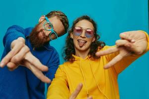 un mujer y un hombre divertido Pareja arrancando y demostración señales con su manos sonriente alegremente, en un azul fondo, el concepto de un real relación en un familia. foto