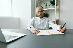 A man in a wheelchair, a businessman in the office works at a laptop, writing down a plan in a notebook, thoughtfulness, integration into society, the concept of working a person with disabilities photo