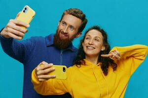 Woman and man funny couple with phones in hand taking selfies crooked smile fun, on blue background. The concept of real family relationships, talking on the phone, work online. photo