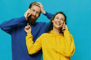 mujer y hombre alegre Pareja con Los telefonos en su manos torcido sonrisa alegre, en azul antecedentes. el concepto de real familia relaciones, hablando en el teléfono, trabajo en línea. foto