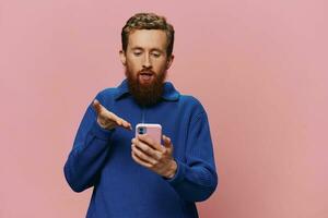 Portrait of a man with a phone in his hands doing looking at it and talking on the phone, on a pink background. Communicating online social media, lifestyle photo
