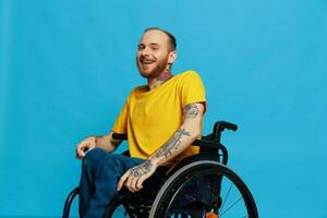 un hombre en un silla de ruedas sonrisa mira a el cámara en un camiseta con tatuajes en su brazos se sienta en un azul estudio fondo, un lleno vida, un real persona foto