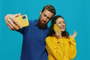 Woman and man funny couple with phones in hand taking selfies crooked smile fun, on blue background. The concept of real family relationships, talking on the phone, work online. photo