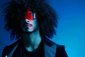 Fashion portrait of a man with curly hair on a blue background wearing red sunglasses, multinational, colored light, trendy, modern concept. photo