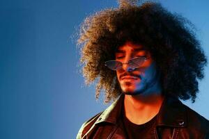 Portrait of a stylish man with curly hair on a blue background multinational, colored light, trendy glasses, modern concept. photo