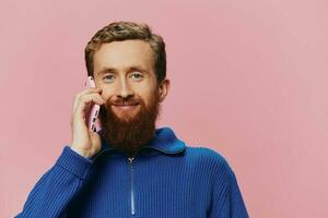 Portrait of a man with a phone in his hands doing looking at it and talking on the phone, on a pink background. Communicating online social media, lifestyle photo