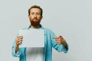 retrato de un adulto masculino en un gris antecedentes con un blanco sábana de papel en su manos para tu diseño y texto, disposición, Copiar espacio, espacio para texto, dedo señalando foto