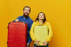 Woman and man smiling, suitcases in hand with yellow and red suitcase smiling merrily and crooked, yellow background, going on a trip, family vacation trip, newlyweds. photo