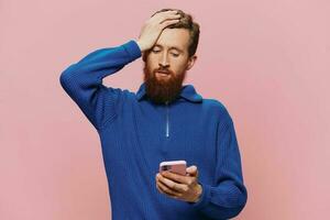 Portrait of a man with a phone in his hands doing looking at it and talking on the phone, on a pink background. Communicating online social media, lifestyle photo