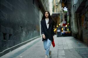 Moda mujer turista en elegante ropa en un chaqueta y rojo boina caminando abajo un estrecho ciudad calle volador pelo y contento viajar, francés estilo, cinematográfico color, retro estilo. foto