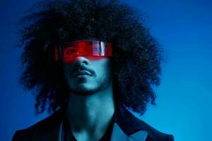 Fashion portrait of a man with curly hair on a blue background wearing red sunglasses, multinational, colored light, trendy, modern concept. photo