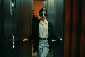 Stylish woman in black jacket and sunglasses posing in elevator, fashion model, dark cinematic light and color, glamor vintage photo