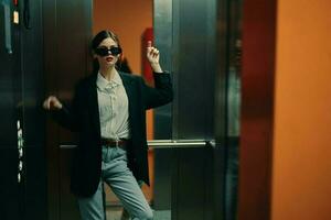 Stylish woman in black jacket and sunglasses posing in elevator, fashion model, dark cinematic light and color, glamor vintage photo