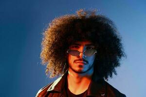 Portrait of a stylish man with curly hair on a blue background multinational, colored light, trendy glasses, modern concept. photo