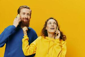 Woman and man cheerful couple with phones in hand talking on cell phone crooked smile cheerful, on yellow background. The concept of real family relationships, talking on the phone, work online. photo