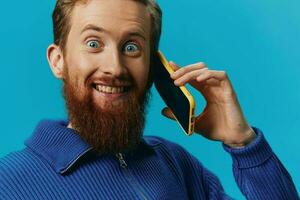 Portrait of a man with a phone in his hands does looking at it and talking on the phone, on a blue background. Communicating online social media, lifestyle photo