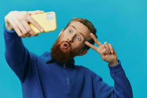 Portrait of a man with a phone in his hands blogger takes selfies, on a blue background. Communicating online social media, lifestyle photo