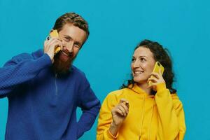 mujer y hombre alegre Pareja con Los telefonos en su manos torcido sonrisa alegre, en azul antecedentes. el concepto de real familia relaciones, hablando en el teléfono, trabajo en línea. foto