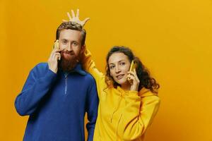 Woman and man cheerful couple with phones in hand talking on cell phone crooked smile cheerful, on yellow background. The concept of real family relationships, talking on the phone, work online. photo