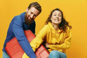 mujer y hombre sonriente, maletas en mano con amarillo y rojo maleta sonriente alegremente y torcido, amarillo fondo, yendo en un viaje, familia vacaciones viaje, recién casados. foto