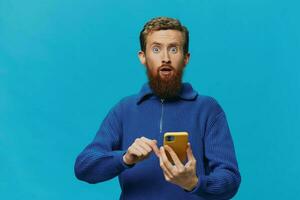 Portrait of a man with a phone in his hands does looking at it and talking on the phone, on a blue background. Communicating online social media, lifestyle photo