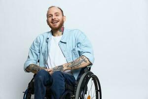 un hombre en un silla de ruedas sonrisa, Copiar espacio, con tatuajes en su brazos se sienta en un gris estudio fondo, el concepto de salud es un persona con discapacidades, un real persona foto