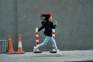 Moda mujer corriendo abajo el calle en frente de el ciudad turista en elegante ropa con rojo labios y rojo boina, viajar, cinematográfico color, retro Clásico estilo. foto