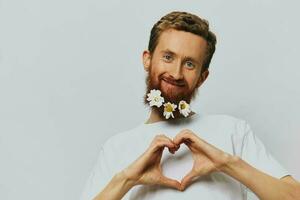 retrato de un gracioso hombre en un blanco camiseta con flores margaritas en su barba en un blanco aislado fondo, Copiar lugar. fiesta concepto y Felicidades. foto