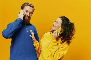 Woman and man cheerful couple with phones in hand talking on cell phone crooked smile cheerful, on yellow background. The concept of real family relationships, talking on the phone, work online. photo