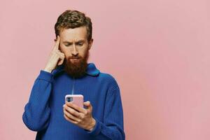 Portrait of a man with a phone in his hands doing looking at it and talking on the phone, on a pink background. Communicating online social media, lifestyle photo