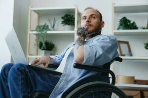 Man wheelchair freelancer working at laptop at home smile, working online, social networks and startup, copy space, integration into society, health concept man with disabilities, real person close-up photo