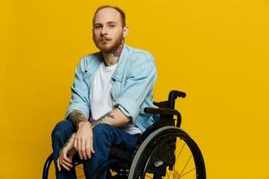 A man in a wheelchair looks at the camera, with tattoos on his arms sits on a yellow studio background, the concept of health is a person with disabilities photo