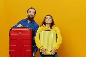 Woman and man smiling, suitcases in hand with yellow and red suitcase smiling merrily and crooked, yellow background, going on a trip, family vacation trip, newlyweds. photo