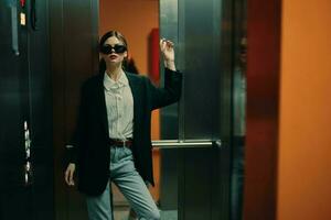 Stylish woman in black jacket and sunglasses posing in elevator, fashion model, dark cinematic light and color, glamor vintage photo